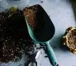 green metal garden shovel filled with brown soil